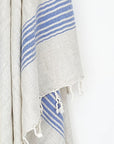Close-up image of a beige linen scarf with a cotton blend and blue colour stripes with knotted fringe.