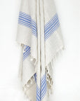 Beige linen scarf with a cotton blend and blue colour stripes with knotted fringe hanging.