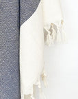 Close-up image of a diamond pattern cotton scarf in navy colour with knotted fringe.