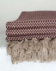 Close-up side image of a burgundy & beige colour cotton blanket with a tasselled edge.