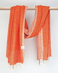 Cotton scarf in orange colour in a 'gentle wave' pattern with knotted fringe and hand-twisted style on the stick.