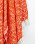 Close-up image of a Cotton scarf in orange colour in a 'gentle wave' pattern with knotted fringe.