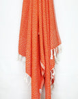 Cotton scarf in orange colour in a 'gentle wave' pattern with knotted fringe hanging.