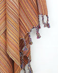 Close-up image of a crochet scarf with a blend of orange colours with knotted fringe.
