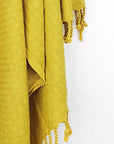 Close-up image of a cotton scarf is handwoven in plain mustard colour with knotted fringe.