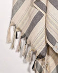 Close-up image of a towel with thin and thick colourful vertical stripes and hand-twisted & knotted fringe.
