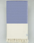 Folded woven cotton blanket with a modern diamond pattern in blue & half part of a beige colour.