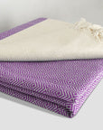 Stylish folded woven cotton blanket with a modern diamond pattern in lilac & half part of a beige colour.