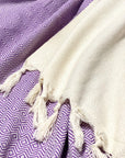 Stylish photo-shooting of a lilac & half part of a beige colour cotton blanket with a knotted fringe.