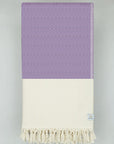 Folded woven cotton blanket with a modern diamond pattern in lilac & half part of a beige colour.