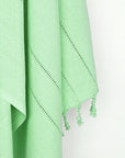Close-up image of a cotton scarf in plain green colour with knotted fringe.
