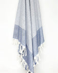 Denim colour towel with white stripes and knotted fringe hanging.