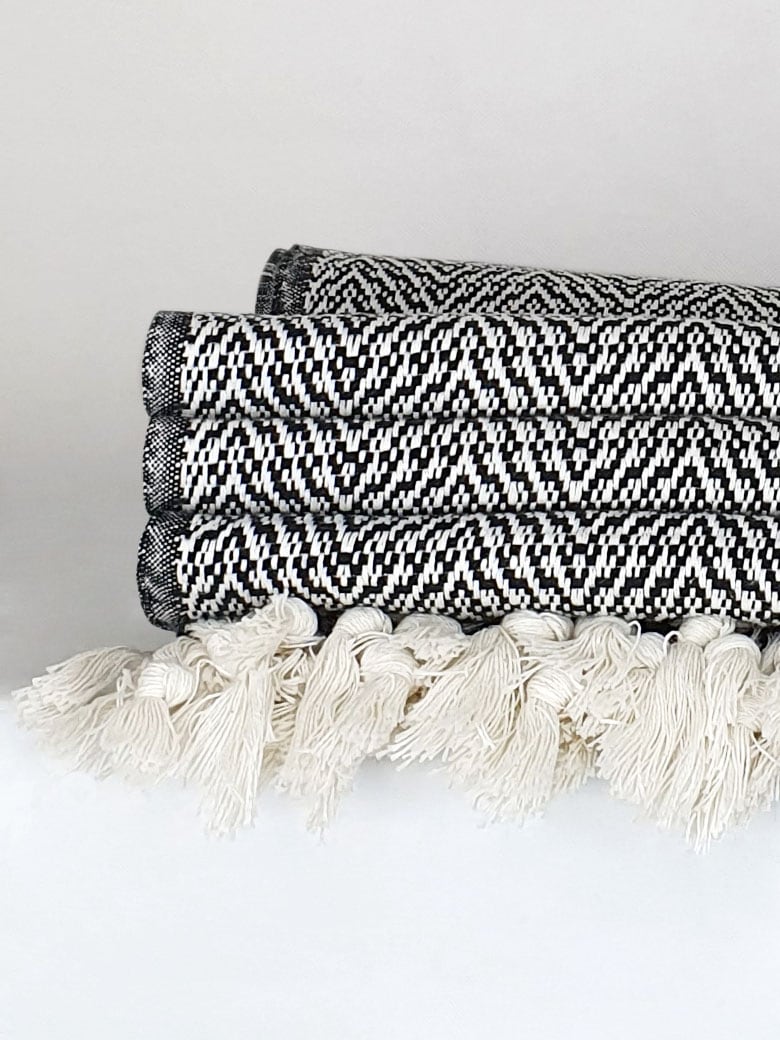 Close-up side image of a black & white colour 100% cotton blanket with a knotted fringe.