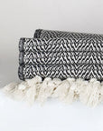 Close-up side image of a black & white colour 100% cotton blanket with a knotted fringe.