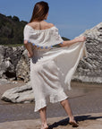 Back image of a woman wearing an off-the-shoulder cream beach dress, tied around the waist, 100% cotton with hand-knitted evil eye detail.