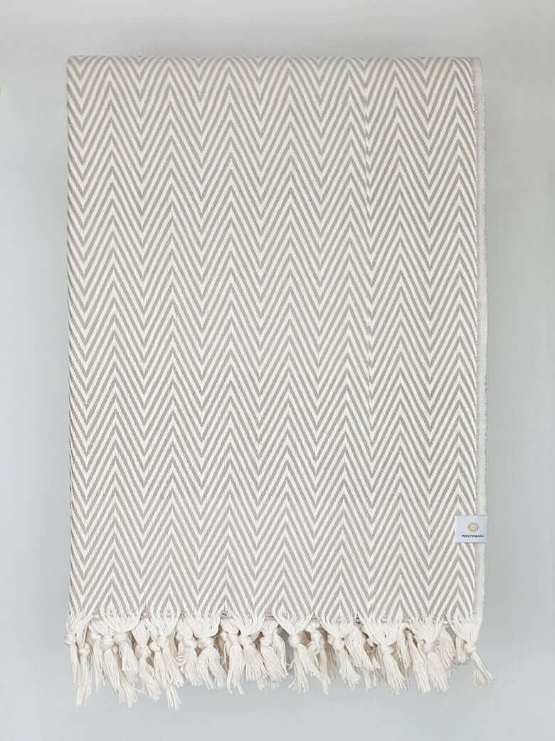 Folded handwoven extra-large blanket with a chevron pattern in beige colour.