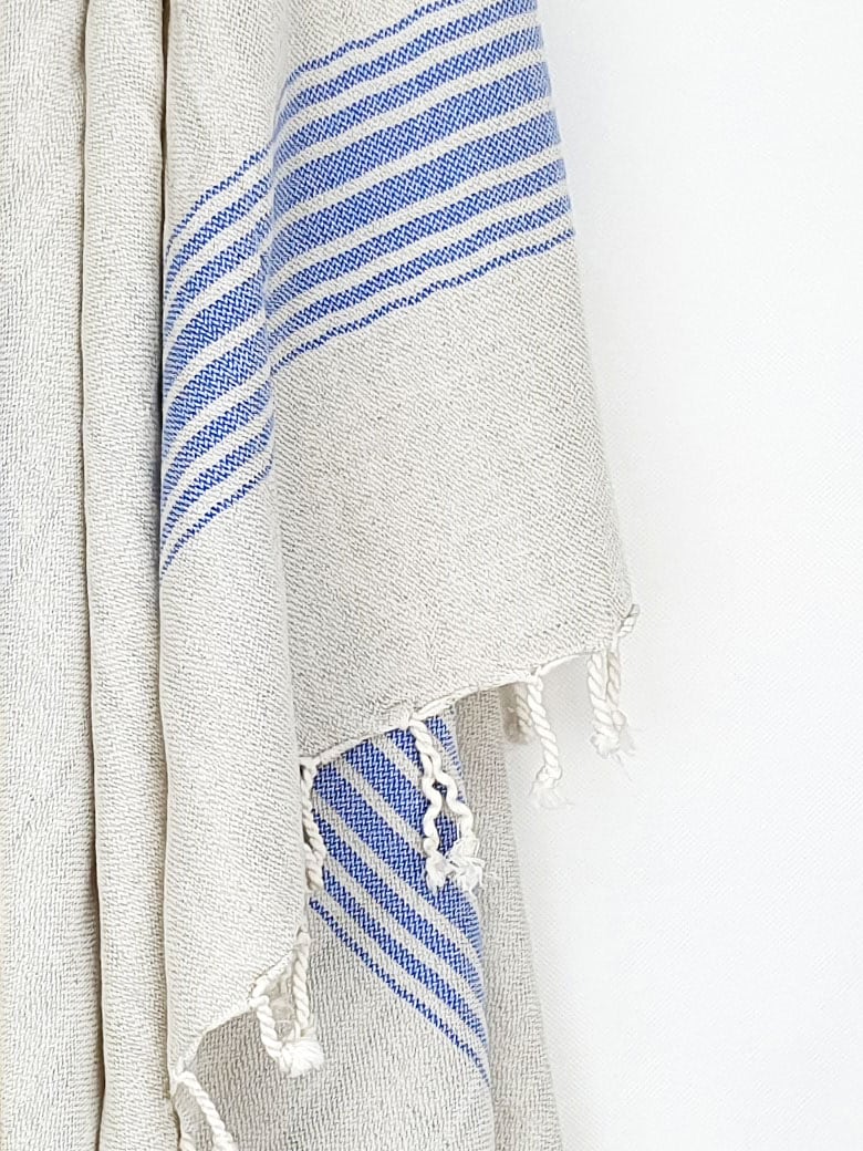 Close-up image of a beige linen scarf with a cotton blend and blue colour stripes with knotted fringe.