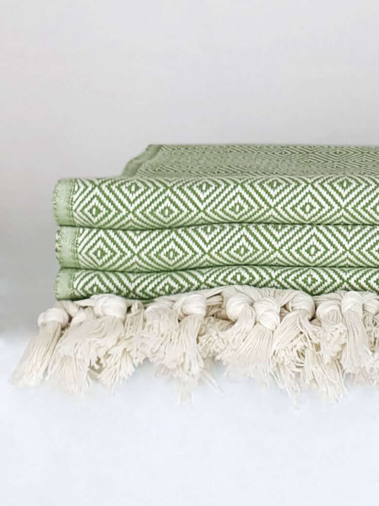 Close-up side image of a green colour large-size blanket with knotted fringe style.