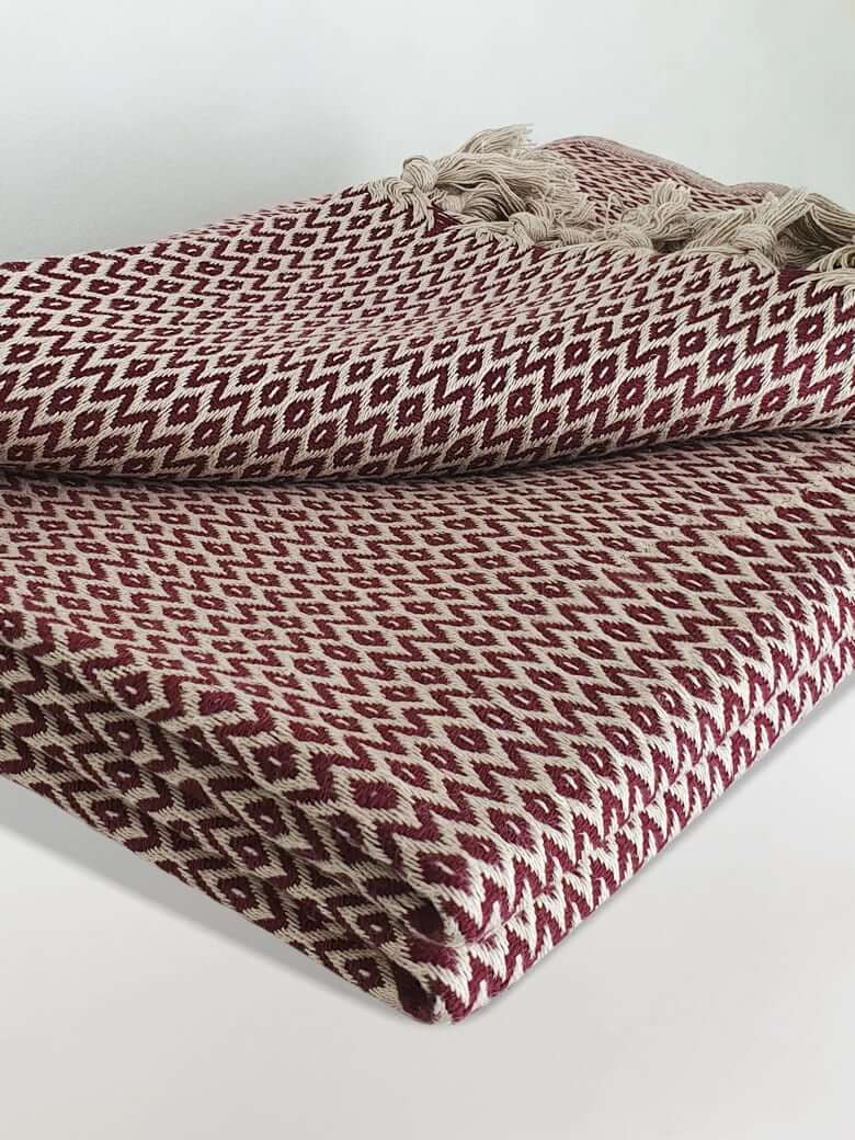 Stylish folded handwoven cotton blanket with an eye-shaped pattern in burgundy & beige colour.