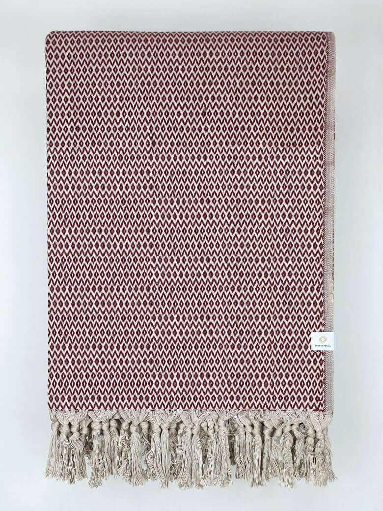 Folded handwoven cotton blanket with an eye-shaped pattern in burgundy & beige colour.