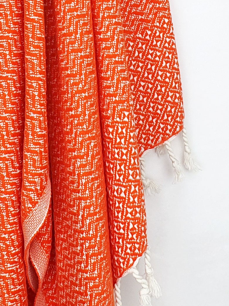 Close-up image of a Cotton scarf in orange colour in a 'gentle wave' pattern with knotted fringe.