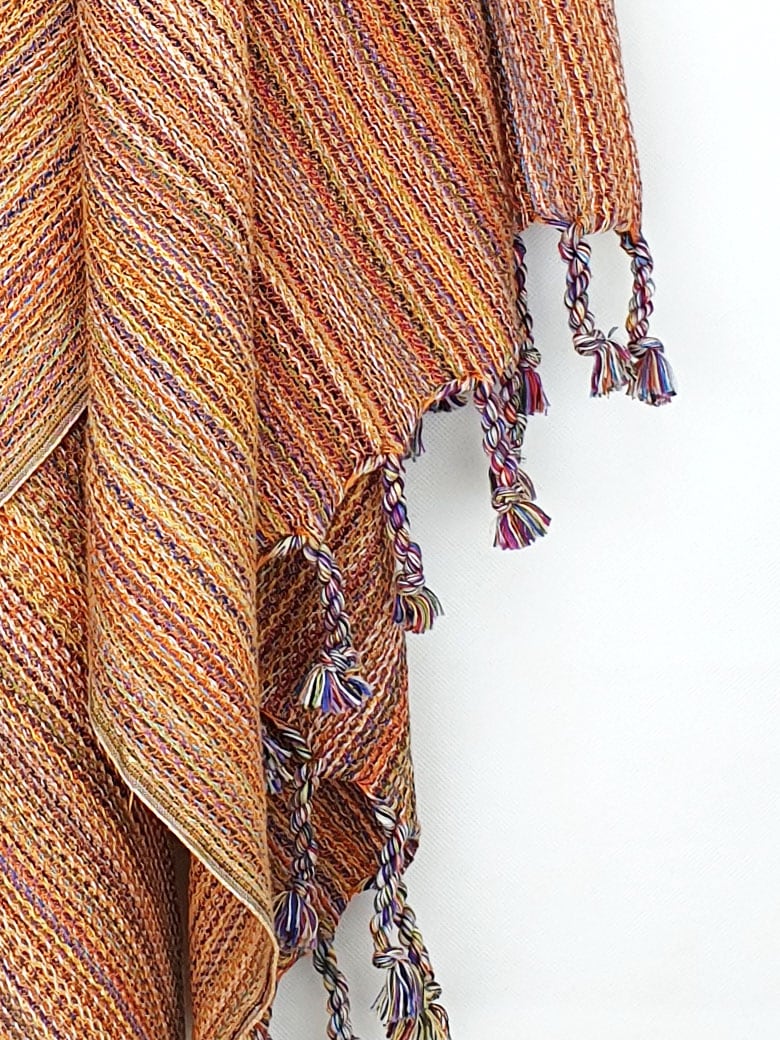 Close-up image of a crochet scarf with a blend of orange colours with knotted fringe.