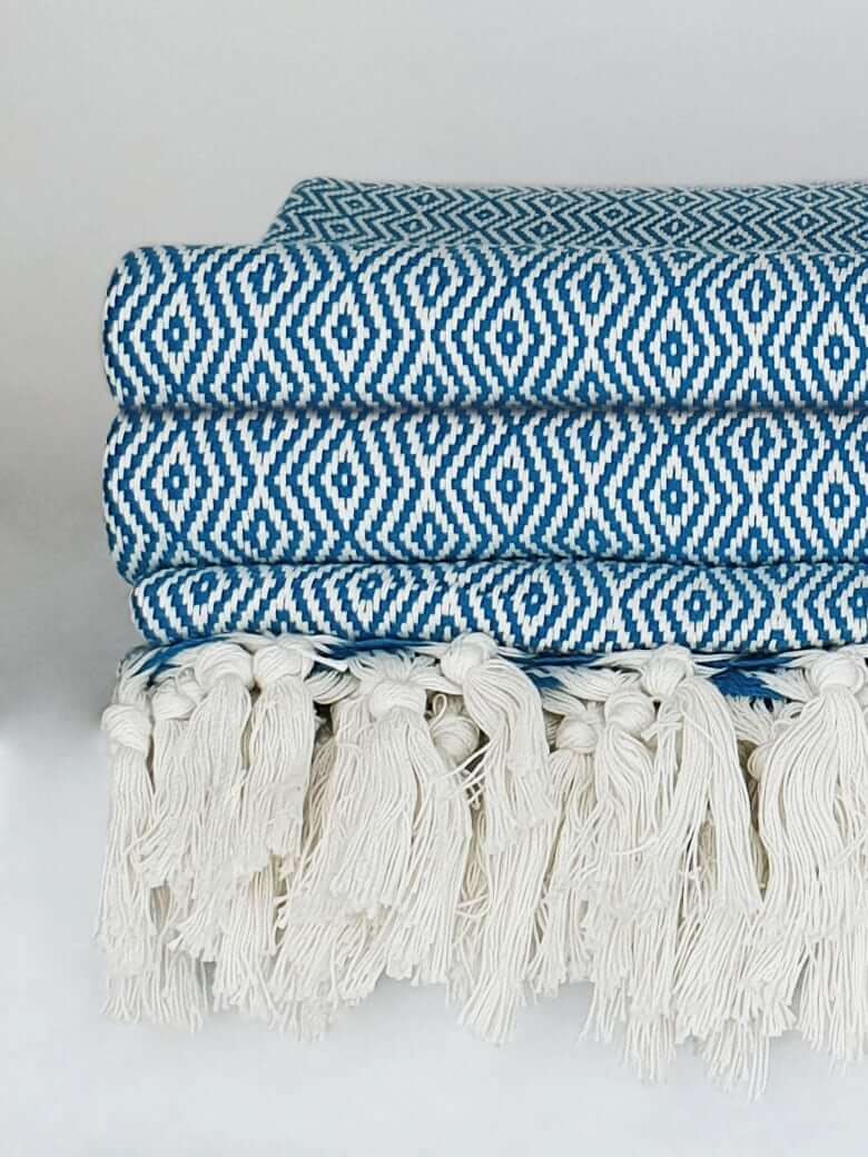 Close-up side image of petrol colour blanket with knotted fringe style.