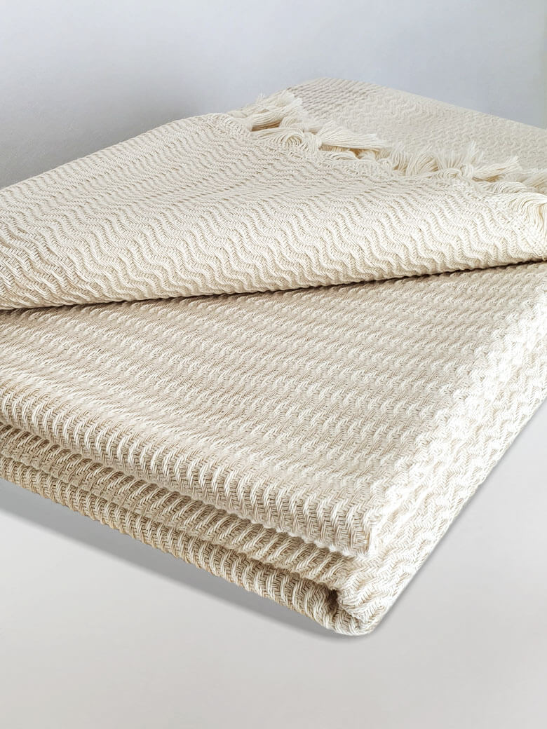 Stylish folded soft cotton blanket with a gentle waves pattern in beige colour.