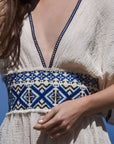 Close-up front image of cream 100% cotton summer maxi dress with v-neck and blue knitted blue patterns around the waist.