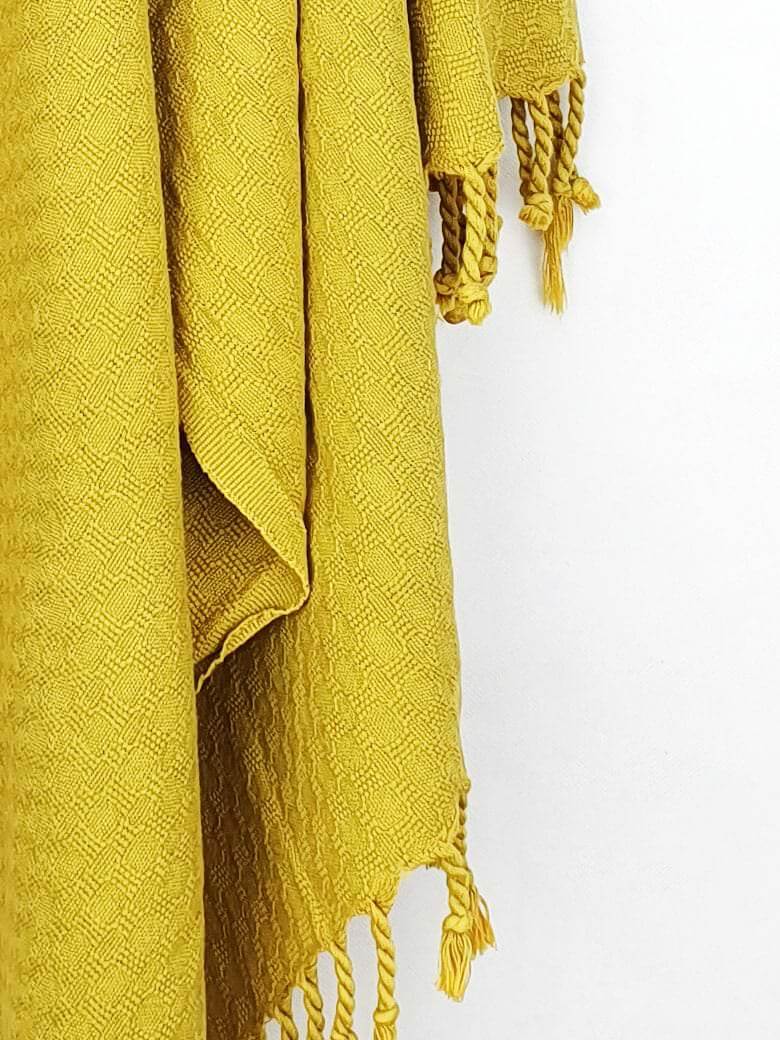 Close-up image of a cotton scarf is handwoven in plain mustard colour with knotted fringe.