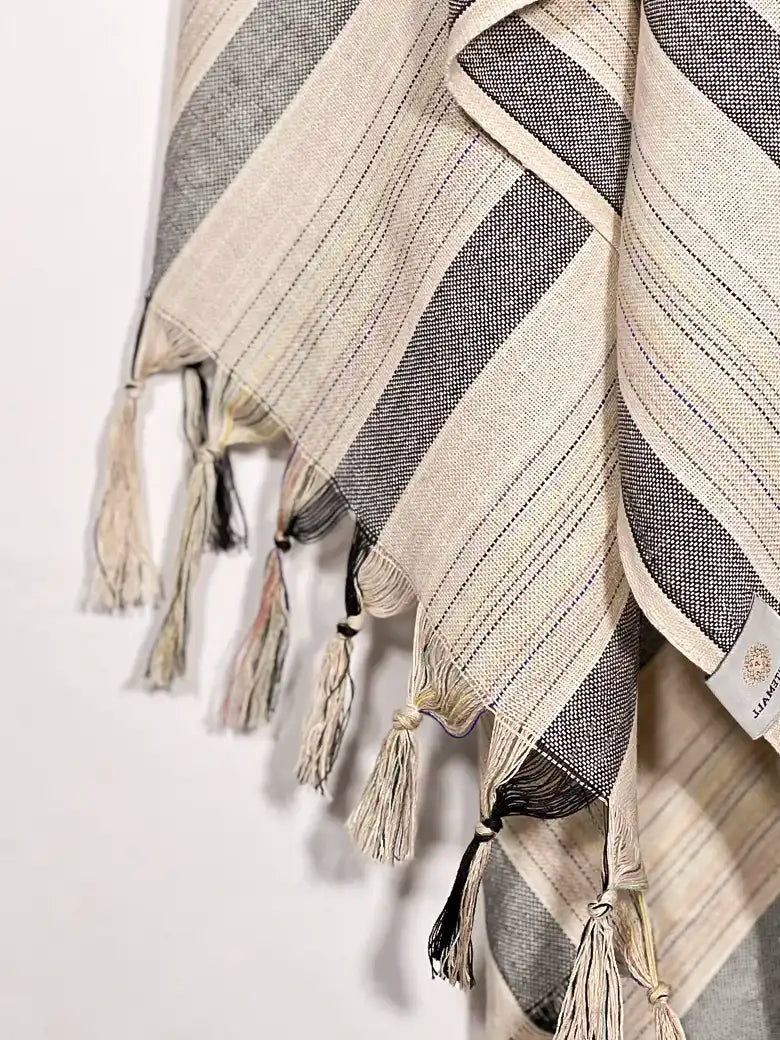 Close-up image of a towel with thin and thick colourful vertical stripes and hand-twisted & knotted fringe.