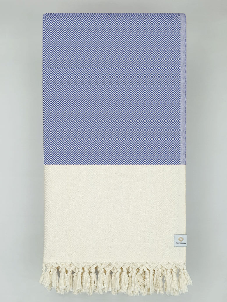 Folded woven cotton blanket with a modern diamond pattern in blue & half part of a beige colour.