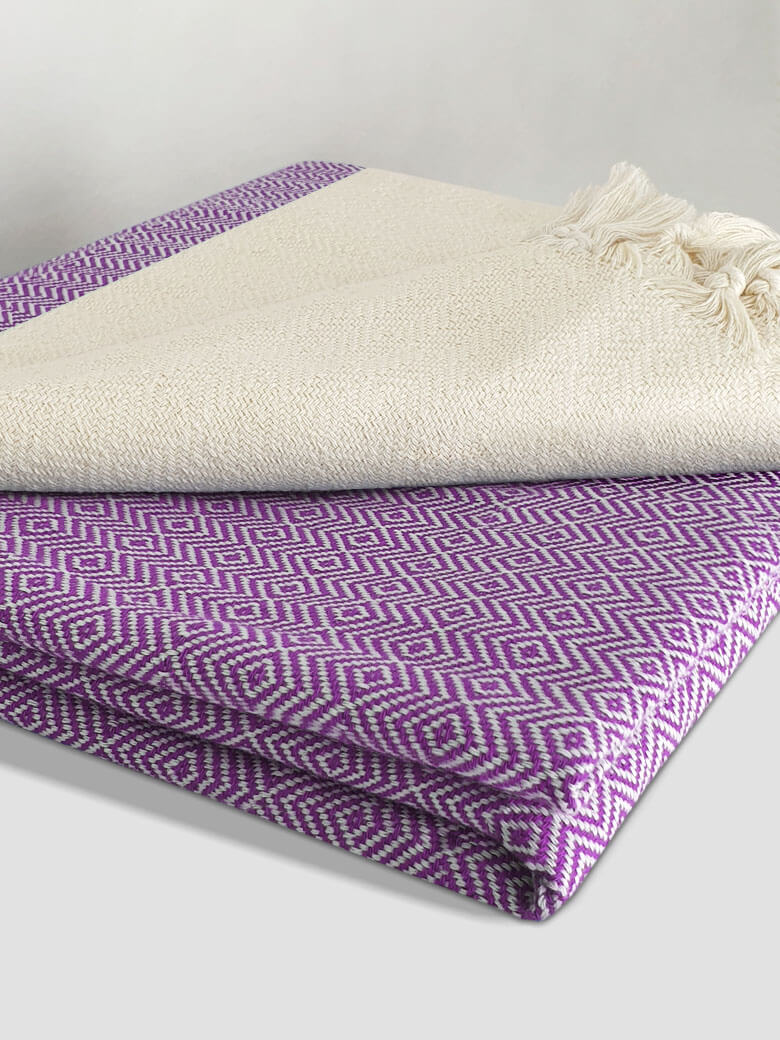 Stylish folded woven cotton blanket with a modern diamond pattern in lilac & half part of a beige colour.