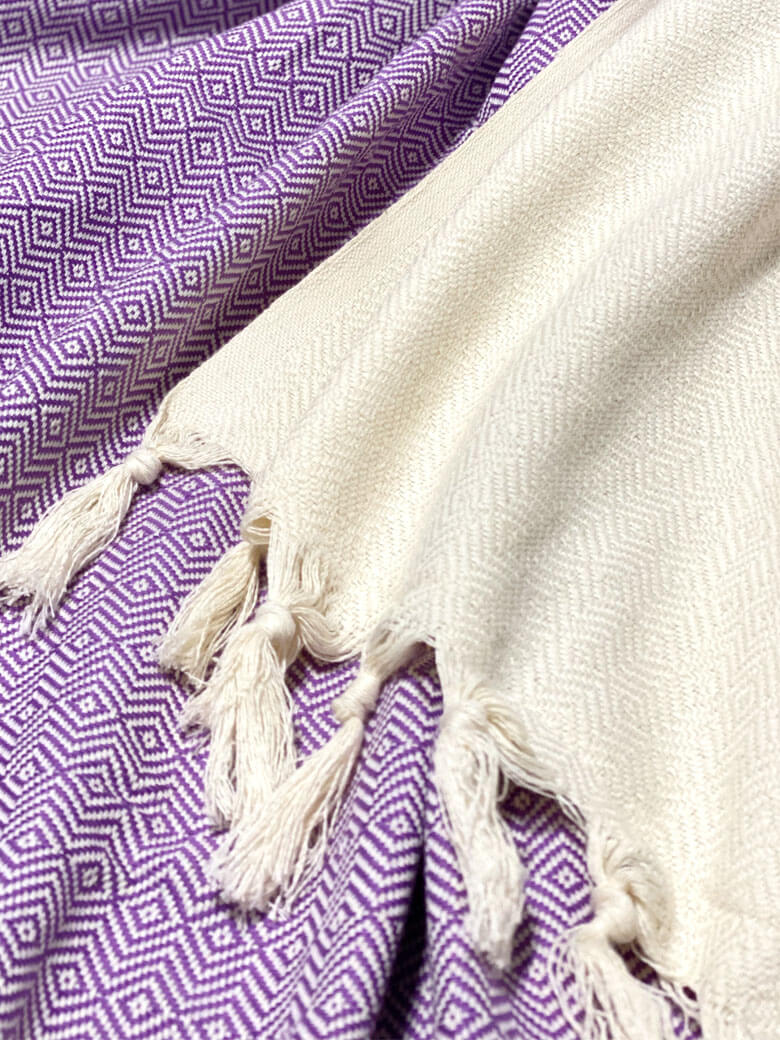 Stylish photo-shooting of a lilac & half part of a beige colour cotton blanket with a knotted fringe.