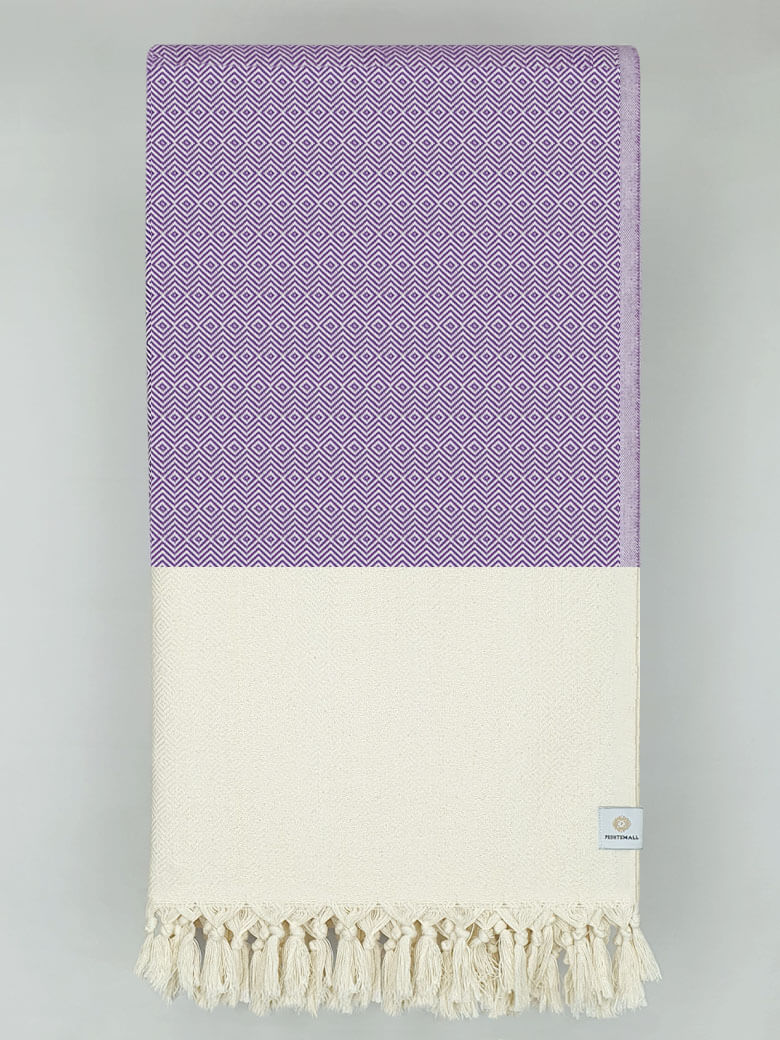 Folded woven cotton blanket with a modern diamond pattern in lilac & half part of a beige colour.