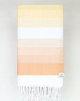Folded a beach towel with stripe orange tonal colours and knotted fringe.