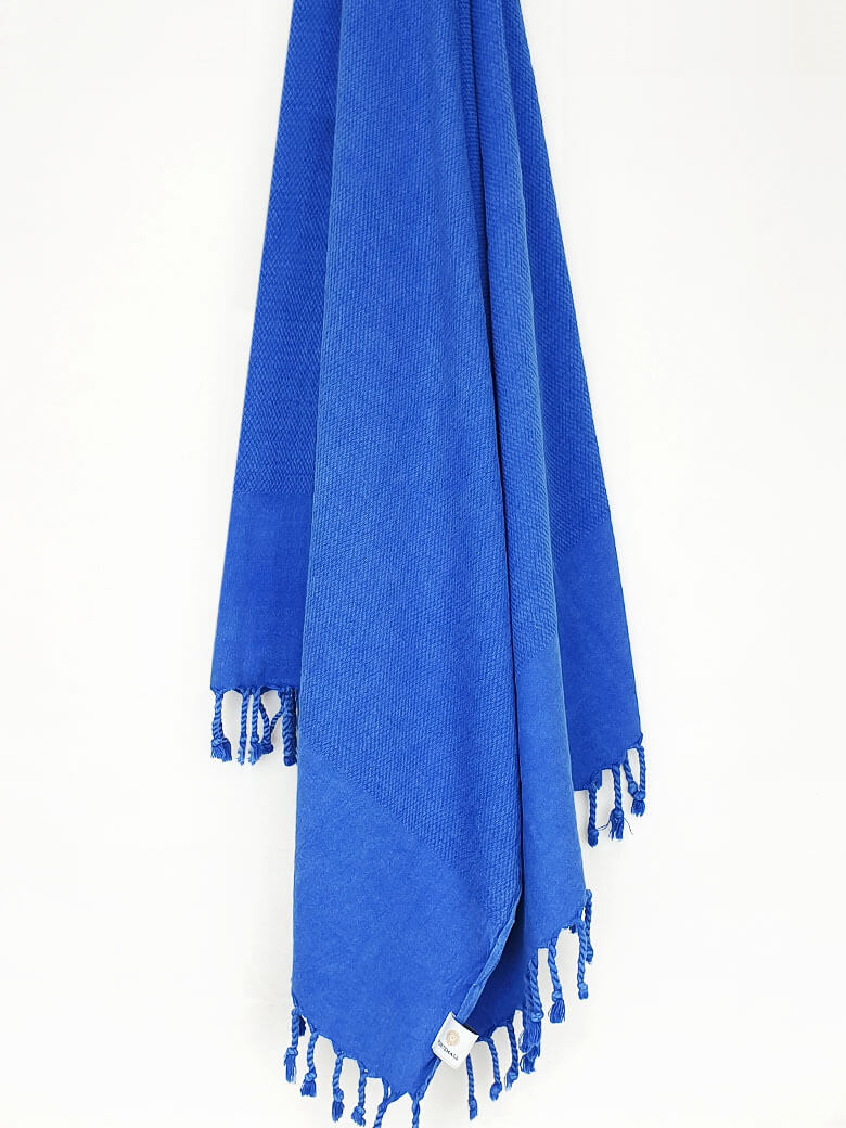 Beach towel in plain blue colour with knotted fringe hanging.