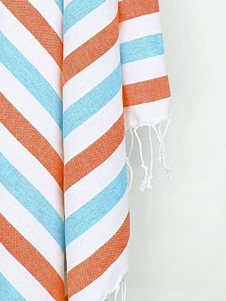 Close-up image of a towel with orange & blue horizontal stripes and hand-twisted & knotted fringe.