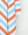 Close-up image of a towel with orange & blue horizontal stripes and hand-twisted & knotted fringe.