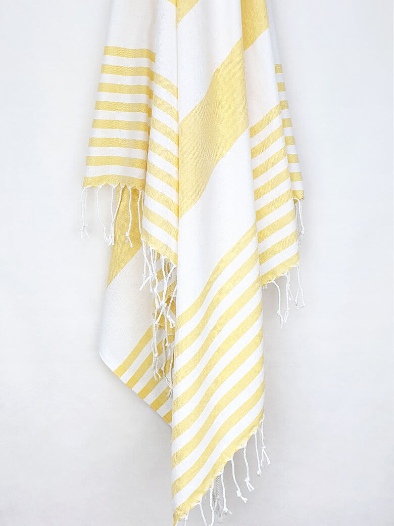 Beach towel with yellow and white colours stripes and knotted fringe hanging.