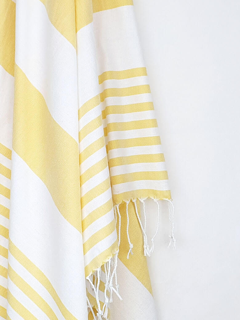 Close-up image of a beach towel with yellow and white colours stripes & knotted fringe.