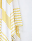 Close-up image of a beach towel with yellow and white colours stripes & knotted fringe.