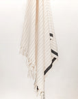 Towel with black stripes on beige colour and knotted fringe hanging.