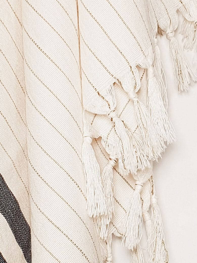 Close-up image of a towel with black stripes on beige colour and knotted fringe.