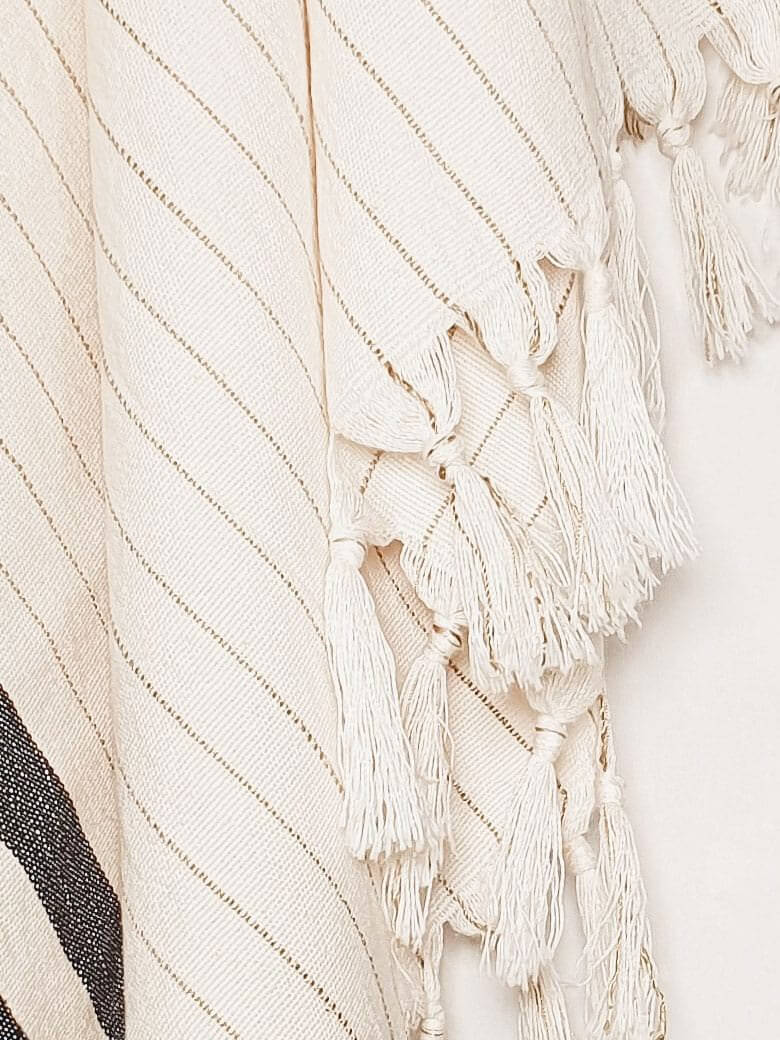 Close-up image of a towel with black stripes on beige colour and knotted fringe.