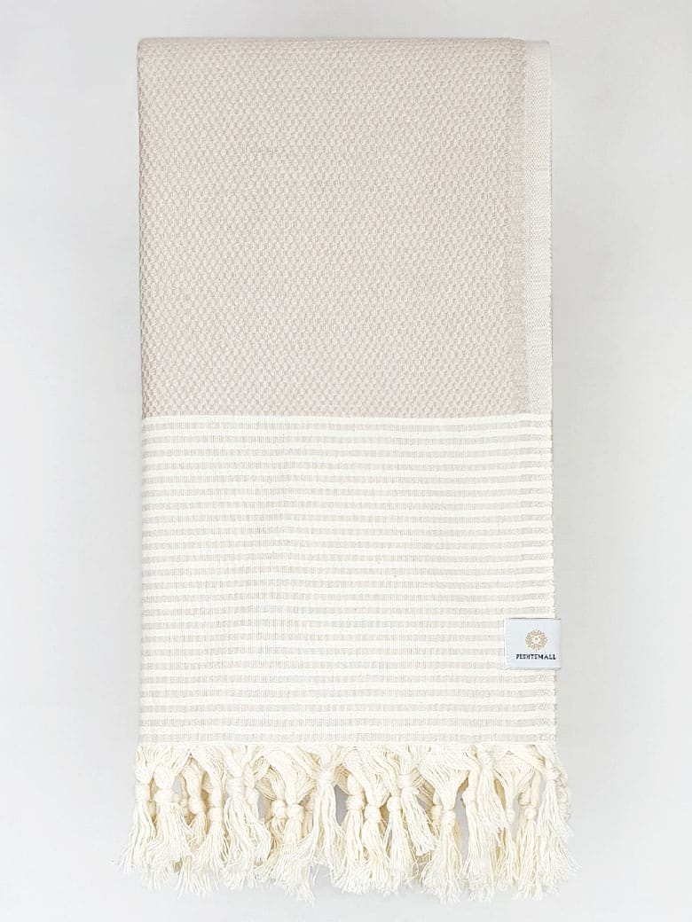 Folded towel in beige colour with horizontal stripes and knotted fringe.