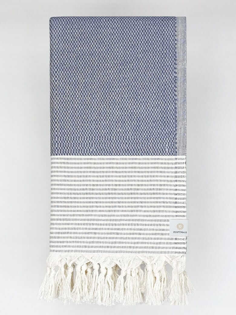 Folded towel in denim colour with horizontal stripes and knotted fringe.