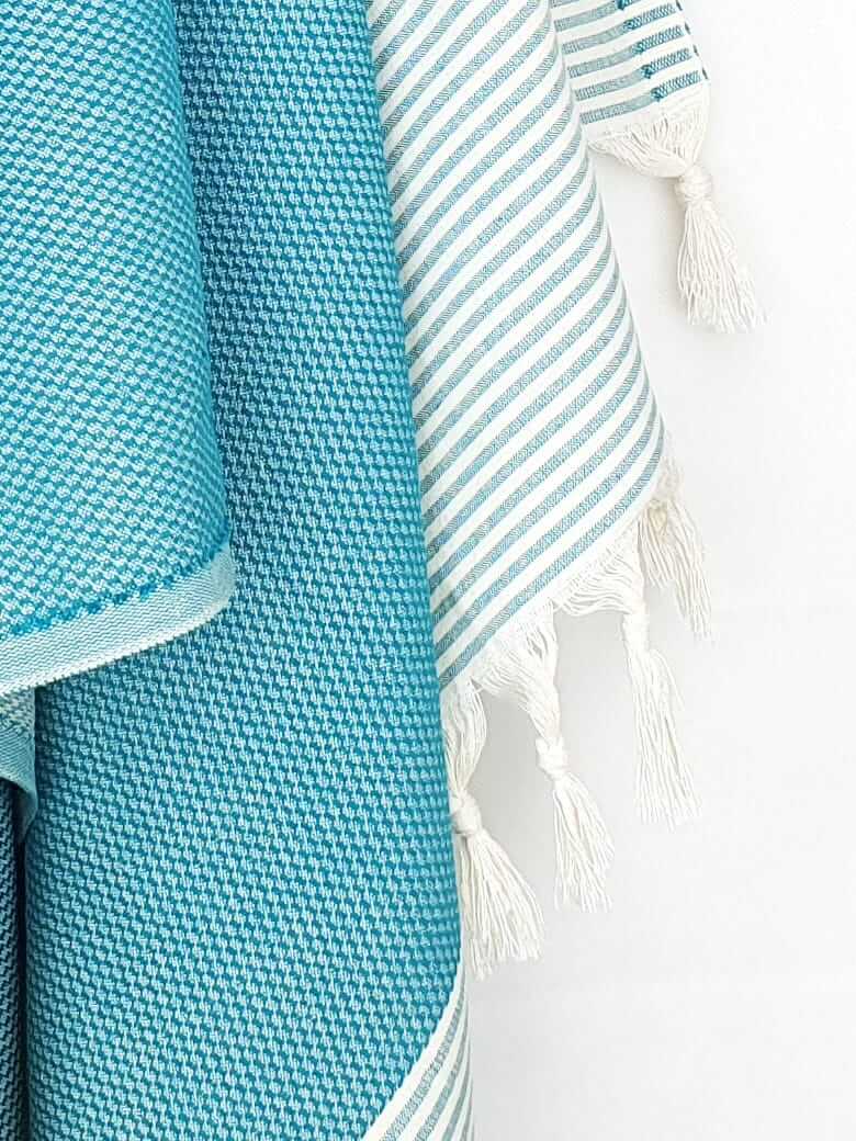 Close-up image of a towel in sea green colour with horizontal stripes and knotted fringe.