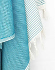 Close-up image of a towel in sea green colour with horizontal stripes and knotted fringe.