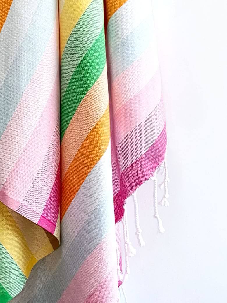 Close-up image of a towel with thick colourful stripes and hand-twisted & knotted fringe.